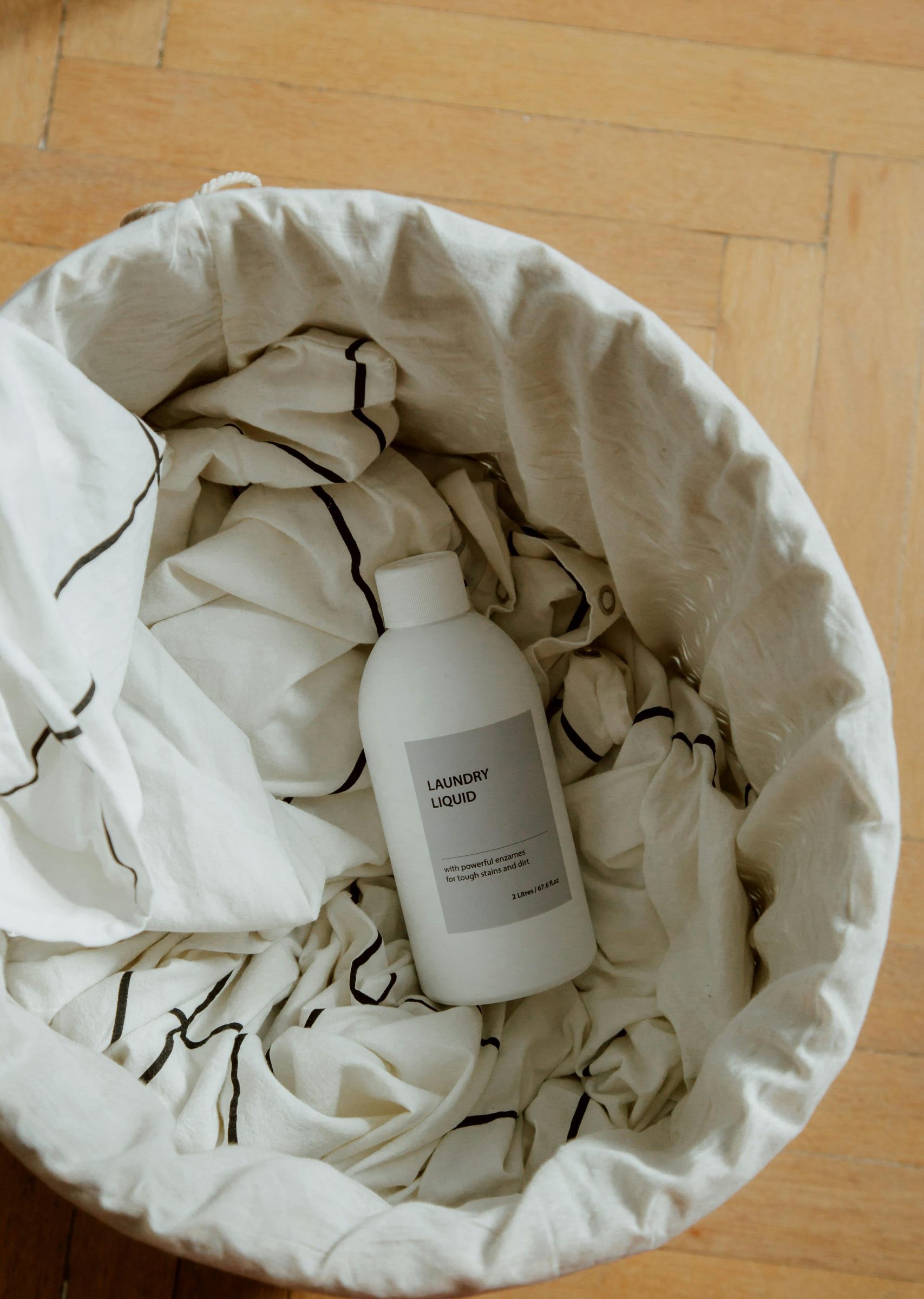Bottle of laundry liquid nestled in a laundry basket filled with cloths on a wooden floor.