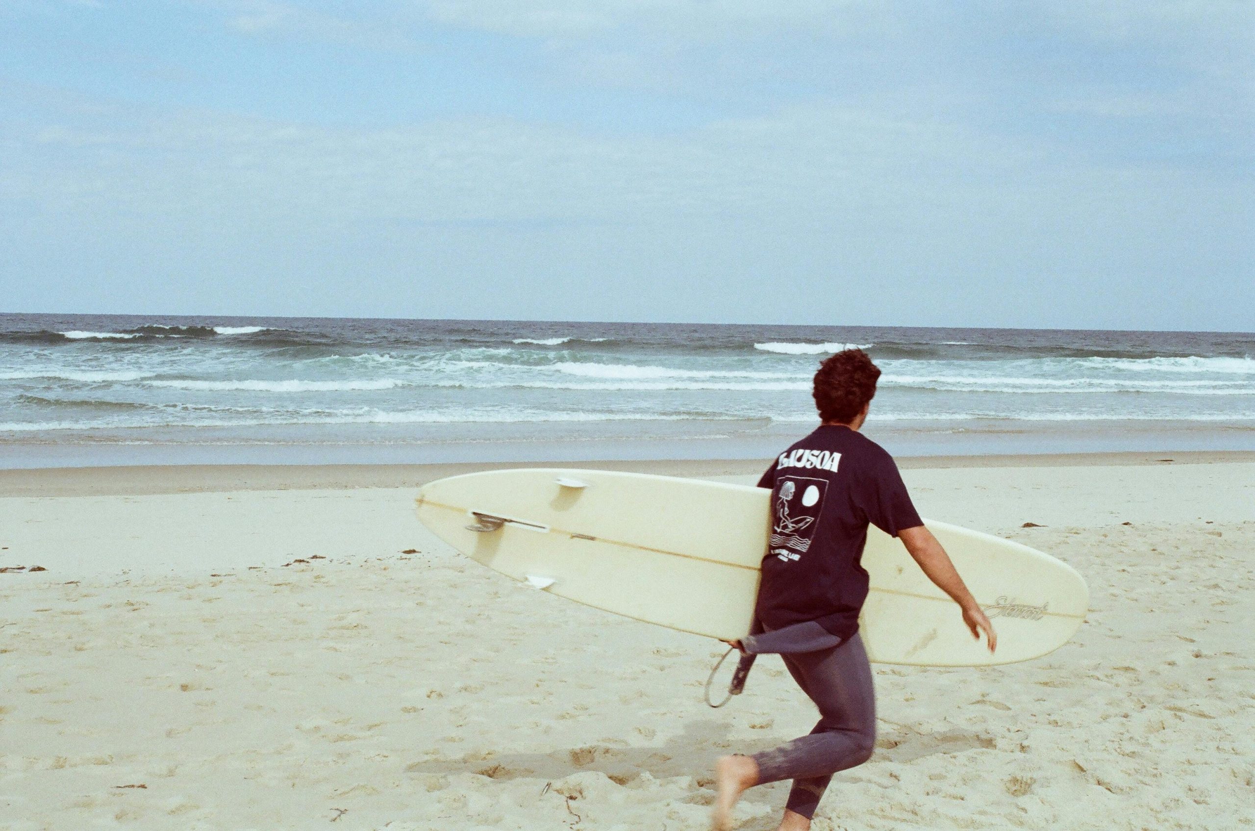 Man running on the beach with a surfboard. Perfect for summer adventure themes.